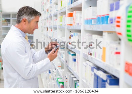 Medium shot of a pharmacist with a digital tablet looking for medication on a pharmacy shelf.