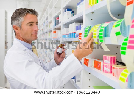 Portrait shot of a pharmacist in an apron reading the labels on a pharmacy shelf.