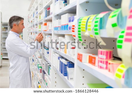 Pharmacist in an apron reading the labels on a pack of medicine from the pharmacy shelf.