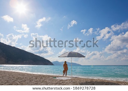 Wide shot of a woman standing under the beach umbrella looking at the view from the beach
