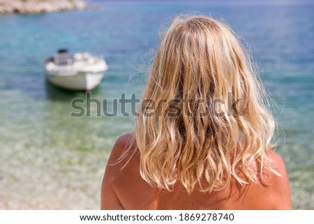 Back shot of a blonde woman looking at the boat in the ocean