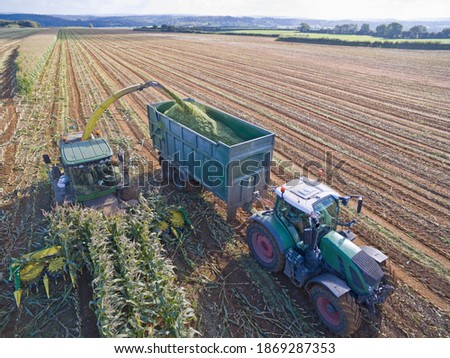 Aerial view of tractor filling trailer with harvested maize in a sunny field