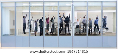 Wide shot through an office window with a group of people jumping in the air.