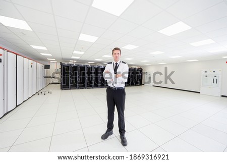 Vertical shot of a security guard standing with his arms crossed in a server room.