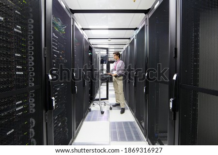 Technician working on a computer while standing in an aisle with server cabinets at a data center.