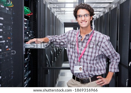Portrait shot of a young technician leaning against a server cabinet in the server room and smiling at the camera.