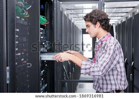 Side view of a young technician replacing a server in the server cabinet.