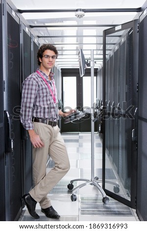 Vertical shot of a young technician standing next to a computer connected to a cabinet in the server room.