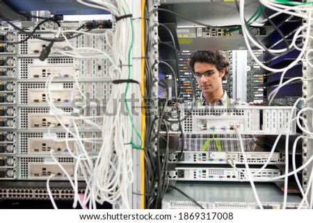 Medium shot of a young technician replacing server drivers in a server cabinet.