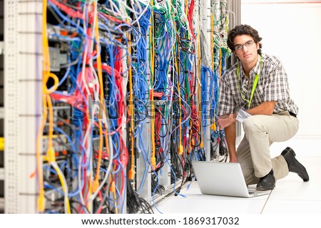 Technician with a laptop kneeling next to a cabinet in the server room of a data center .