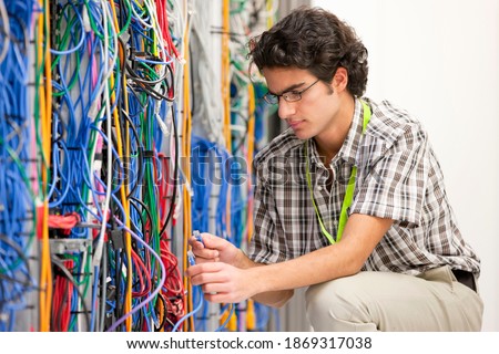 Young technician connecting cables in the server room of a data center.