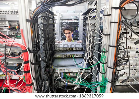 Wide shot of a young technician replacing server drivers in a server cabinet.