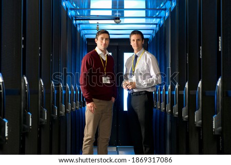 Medium shot of a manager and technician standing in the aisle of a server room at a data center.