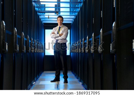 Full shot of a manager standing in the aisle of a server room at a data center.