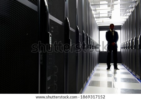 Wide shot of a manager standing in the aisle of a data center aligned with storage cabinets.