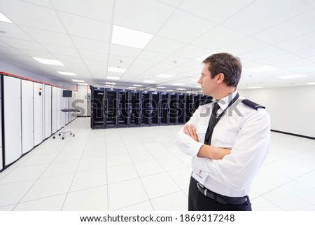 Medium shot of a security guard standing with his arms crossed in a server room.