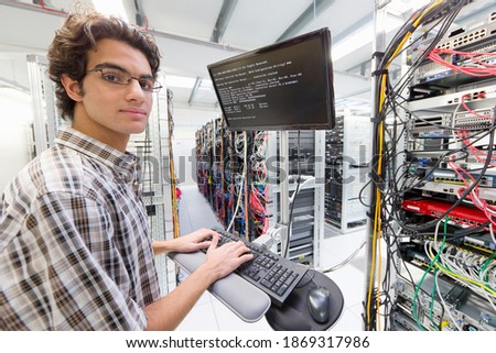Technician looking at the camera while working on a computer in a server room at a data center.