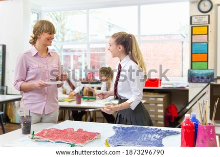 An art teacher guiding a middle school student during an art class.