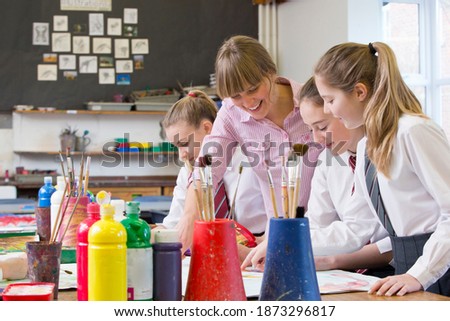 Medium shot of an art teacher helping middle school students during an art class.
