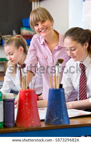 Vertical shot of an art teacher helping middle school students and smiling at the camera.