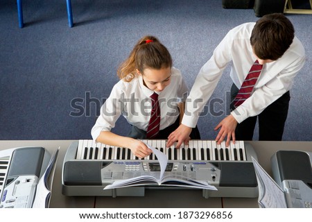High angle shot of a high school girl playing a piano in a music class with a classmate assisting her.