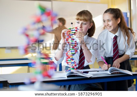 High school girl assembling a helix DNA model in a science class with her classmate standing next to her.