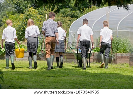 Back shot of Teacher and middle school students with wheelbarrow learning gardening in vegetable garden