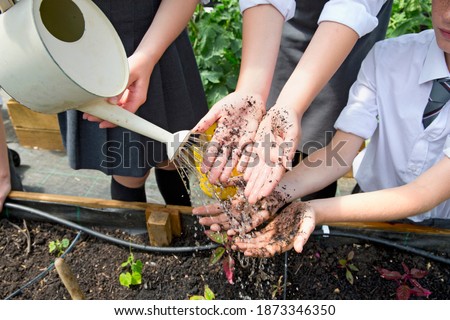Middle school students washing dirty hands with a watering can during gardening lessons