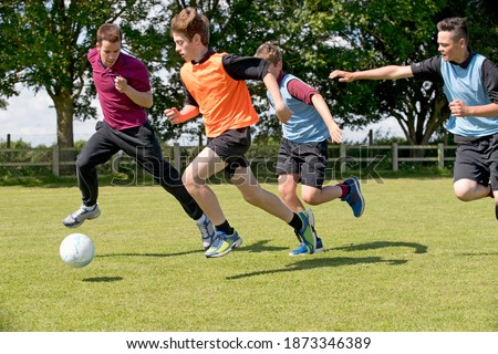 Middle schoolboys and teacher running while playing soccer on the field in physical education
