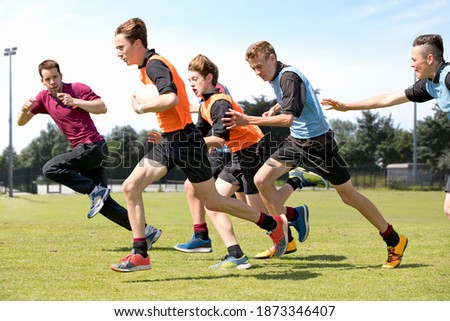 Middle schoolboys and teacher running while playing rugby on the field in physical education class