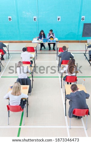 Teachers supervising middle school students taking examination at desks in school gymnastics hall