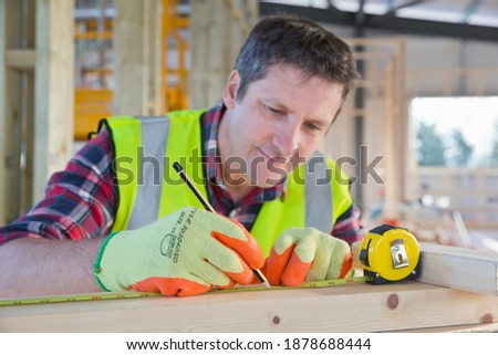 Close up of a Carpenter making markings on the wooden planks at a construction site in a building wearing a high visibility safety vest