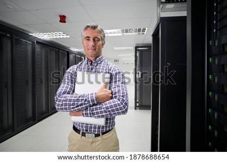 Portrait Of a Technician standing With Laptop held in crossed arms In the secured data center