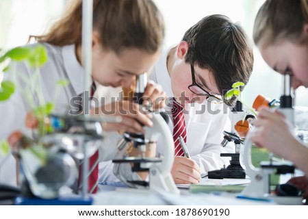 High school students making notes while conducting scientific experiment using microscopes in a biology class.