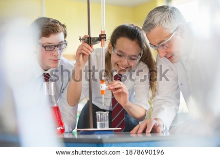 Chemistry teacher watching high school students conduct a scientific experiment using a dropper.