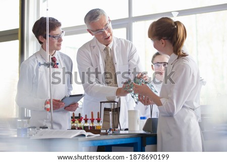 Chemistry teacher and high school students conducting a scientific experiment using a model.
