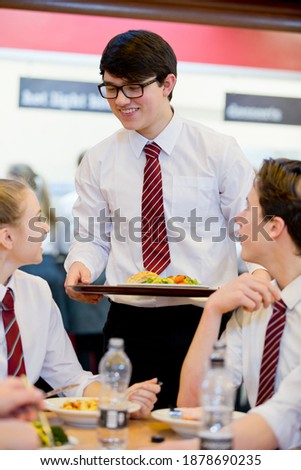 Vertical shot of a male high school student standing next to his friends eating lunch in the school cafeteria.