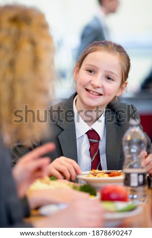 Vertical shot of a middle school student eating lunch and talking to a friend in the school cafeteria.