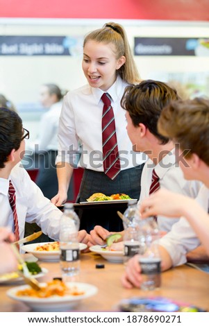 Vertical shot of a female high school student standing next to her friends eating lunch in the school cafeteria.