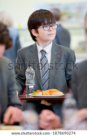 Portrait shot of a middle school student walking with his lunch in the school cafeteria.