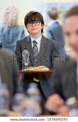 Vertical shot of a middle school student walking with his lunch in the school cafeteria.