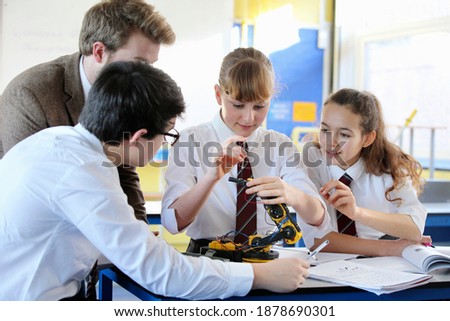 A group of high school students assembling a robot during a science class with a teacher assisting them.