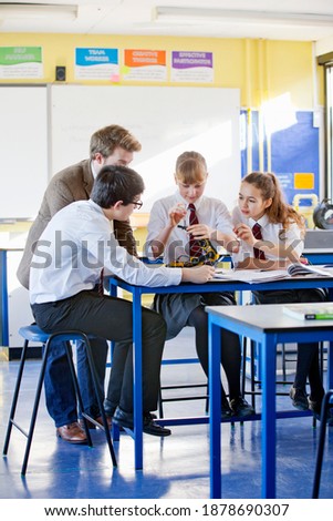 Vertical shot of a group of high school students assembling a robot during a science class with a teacher assisting them.