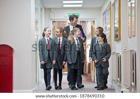Full shot of a teacher talking to middle school students while walking through a school corridor.