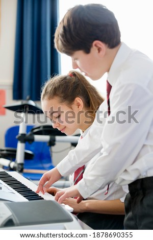 Vertical shot of a high school student helping a classmate play piano during a music class.