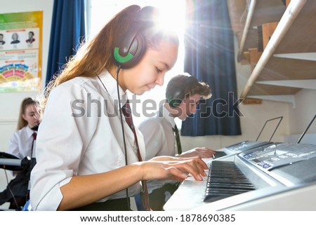 High school students with headphones playing piano in a music class.