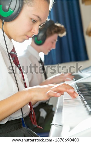 Vertical shot of female high school student with headphones playing piano in a music class.