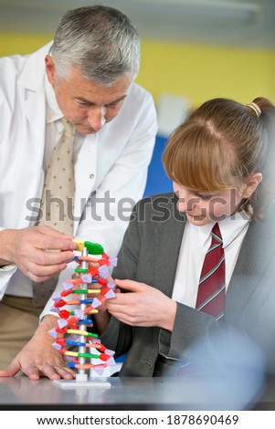 Vertical shot of a science teacher helping a high school student assemble a helix DNA model.