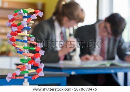 Helix DNA model with high school student conducting a scientific experiment in the background.