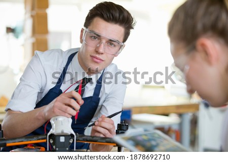 Portrait shot of a high school boy looking at the camera while testing the electronics of a drone in a shop class.